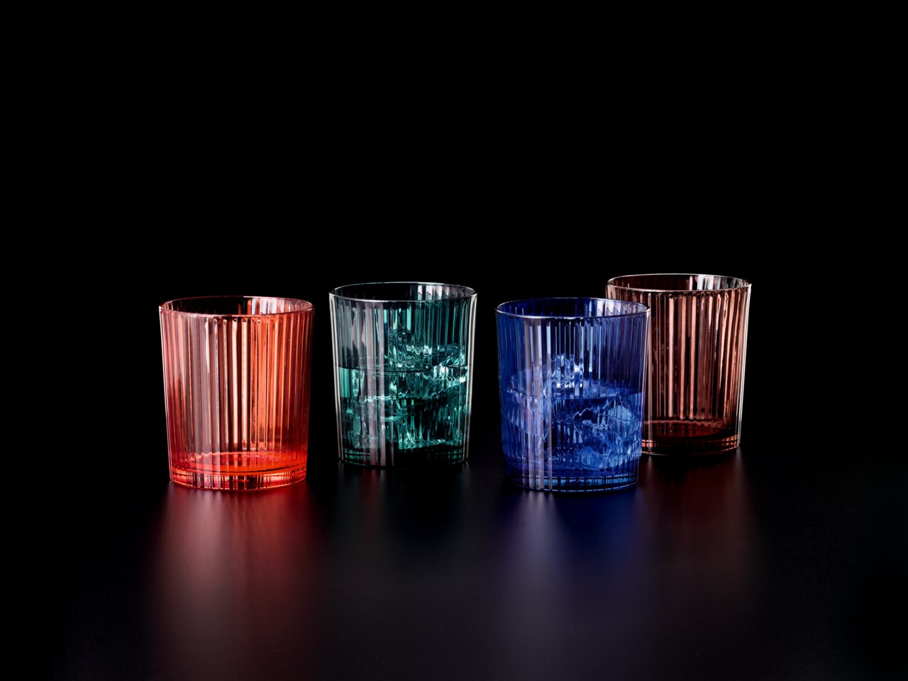 Vier bunte, geriffelte Becher aus Glas in Rot, Grün, Blau und Rosa auf schwarzem Hintergrund, seitliche Perspektive.