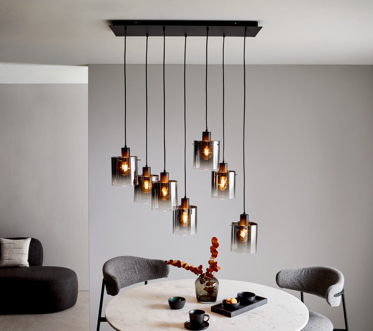 Moderne Hängeleuchte mit mehreren Glaskörpern, die von der Decke hängen, in einem stilvoll eingerichteten Esszimmer. Perspektive von schräg unten.