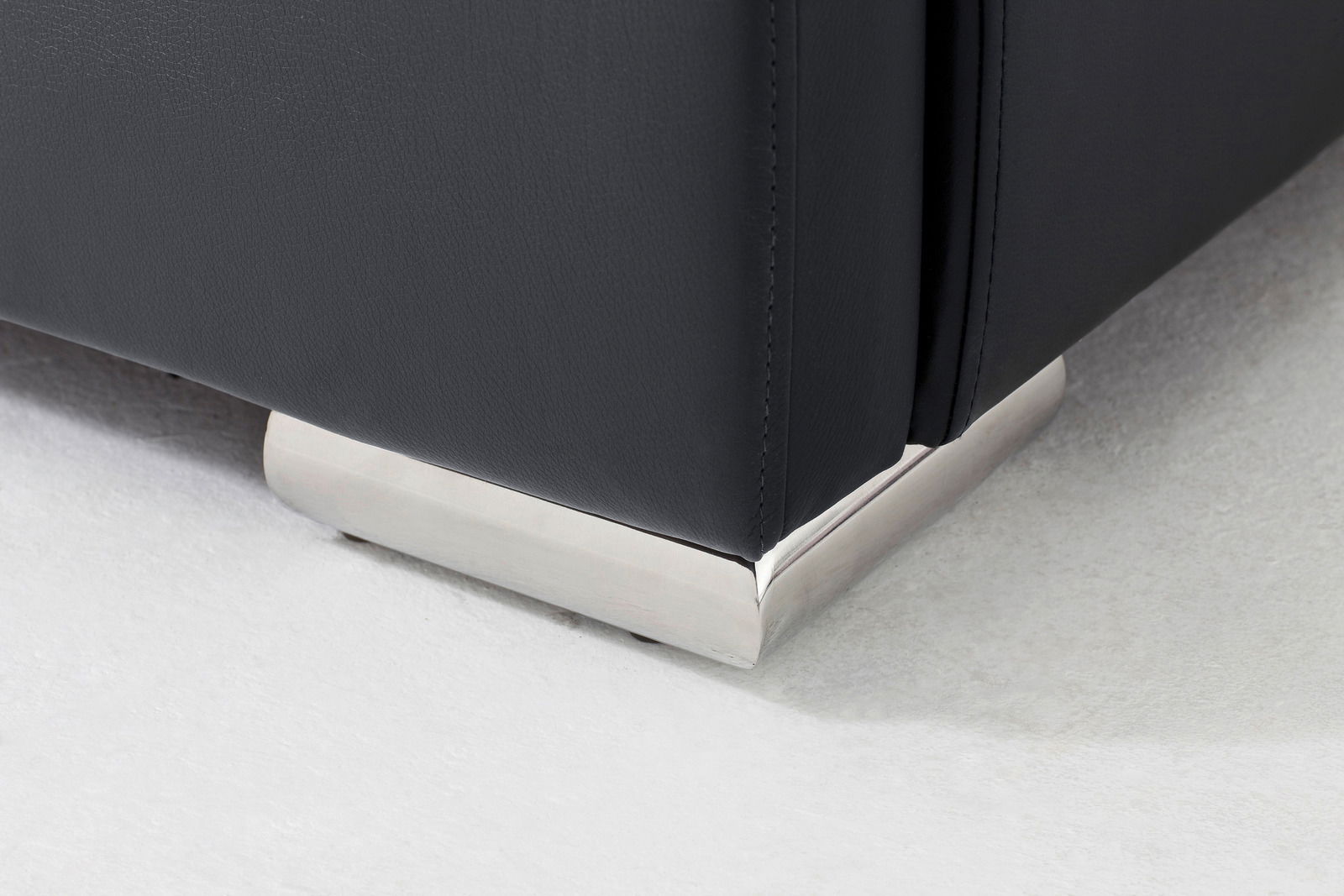 Nahaufnahme eines Polsterbettfußes aus Metall mit schwarzem Bezug, von der Seite betrachtet.