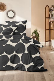Bettwäsche-Set mit großem, schwarzem Kreismuster auf weißem Hintergrund, im Schlafzimmer mit Holzboden und Pflanzen dekoriert, aus der Perspektive von vorne.