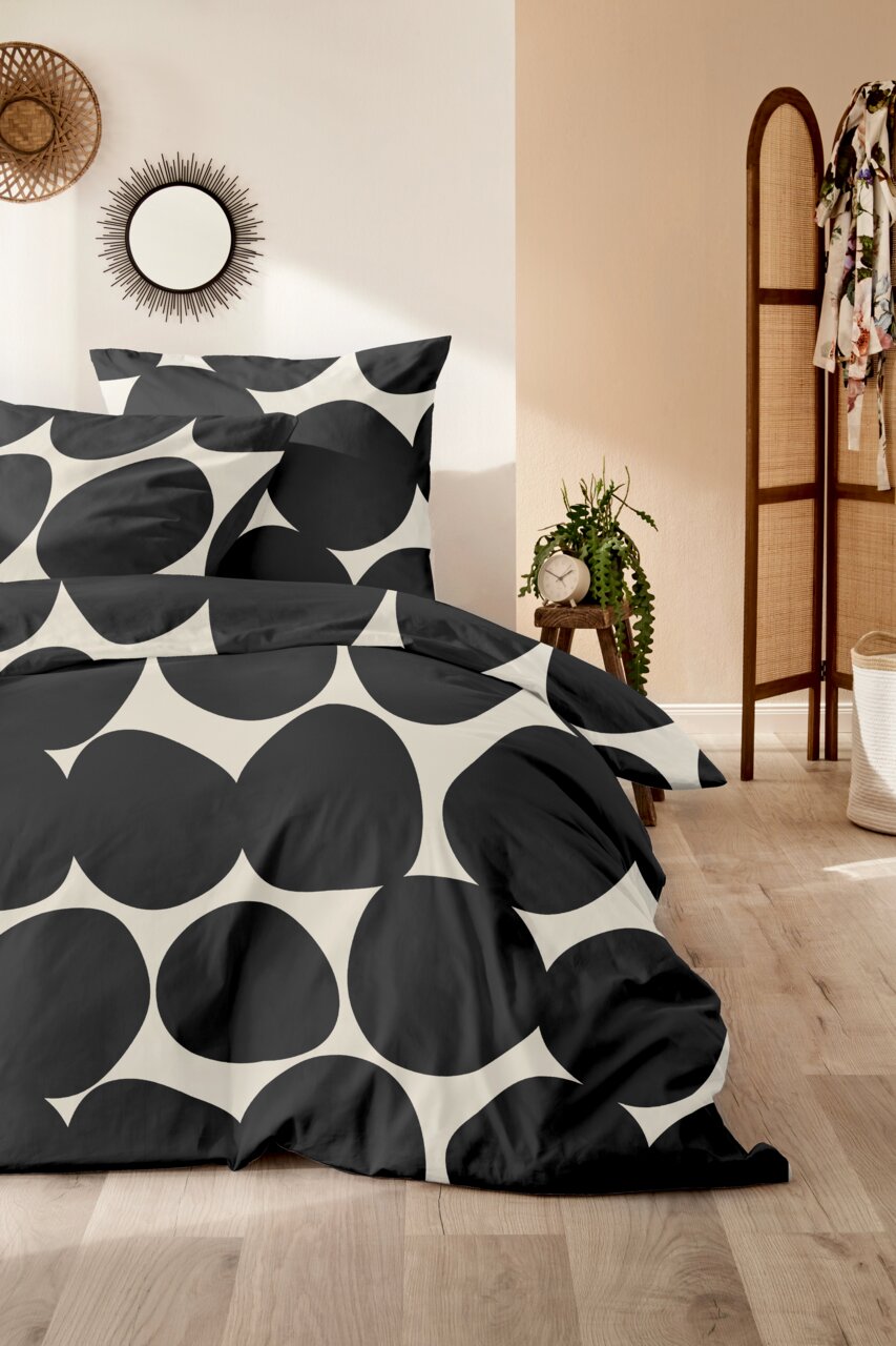 Bettwäsche-Set mit großem, schwarzem Kreismuster auf weißem Hintergrund, im Schlafzimmer mit Holzboden und Pflanzen dekoriert, aus der Perspektive von vorne.