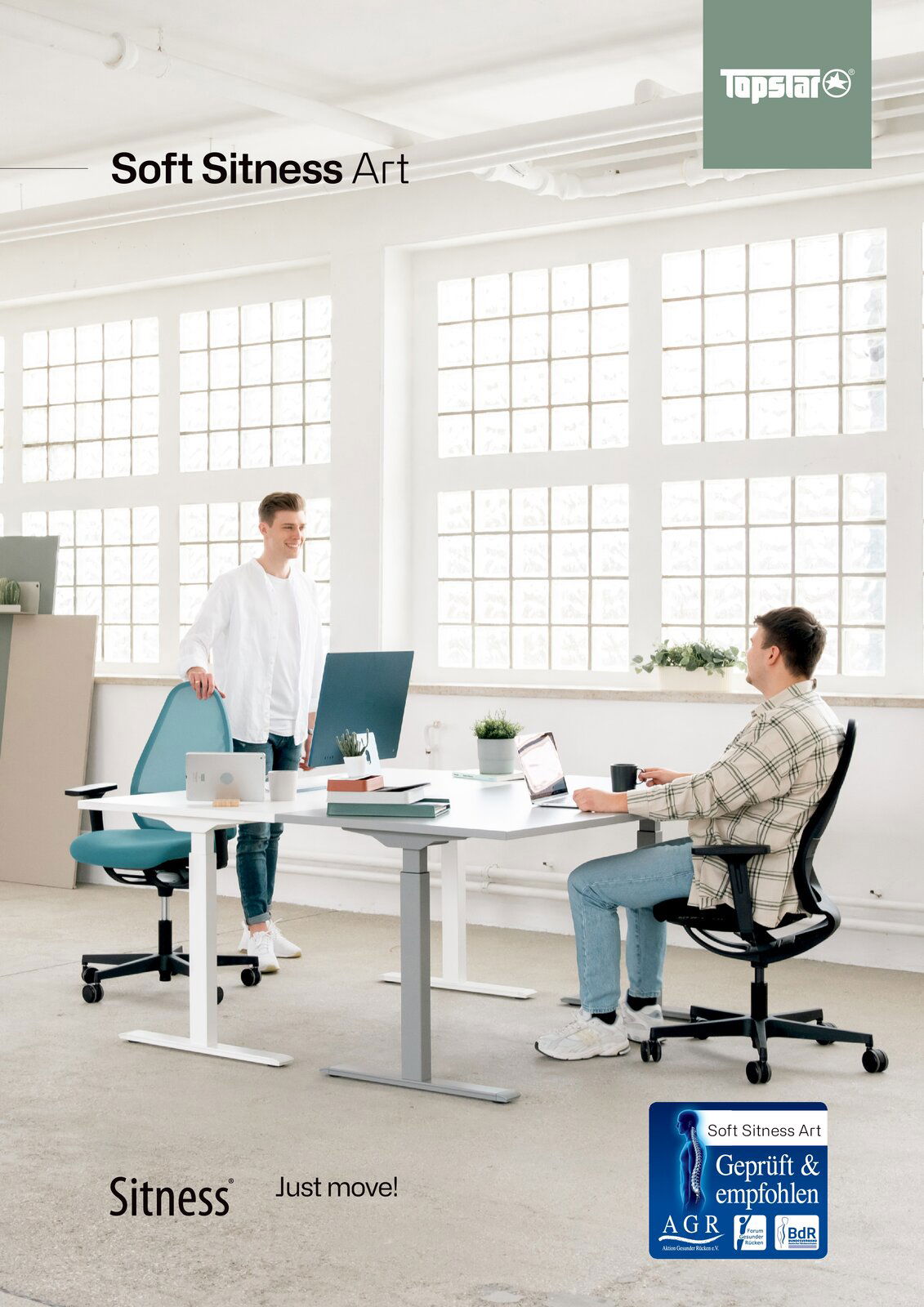 Zwei Männer in einem modernen Büro mit großen Fenstern, die an einem weißen Schreibtisch arbeiten. Einer sitzt auf einem schwarzen Bürostuhl, der andere steht neben einem türkisfarbenen Bürostuhl. Perspektive von vorne.