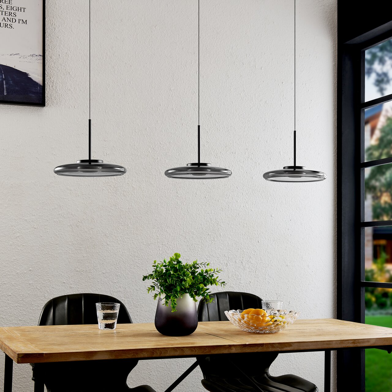 Moderne LED-Hängeleuchte in dreifacher Ausführung über einem Esstisch, seitliche Perspektive.