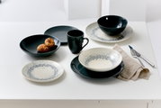 Tafelservice Cecina Graphit 18-teilig, bestehend aus Tellern, Schalen und Tassen in einem modernen Design mit grauen und weißen Akzenten, auf einem Tisch von oben fotografiert.