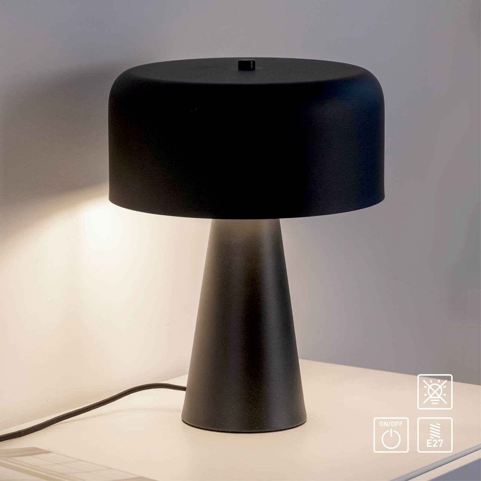 Schwarze moderne Tischleuchte mit breitem, abgerundetem Lampenschirm und konischem Fuß auf einem Tisch, warm leuchtend, frontal aus leicht erhöhter Perspektive fotografiert