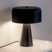Schwarze moderne Tischleuchte mit breitem, abgerundetem Lampenschirm und konischem Fuß auf einem Tisch, warm leuchtend, frontal aus leicht erhöhter Perspektive fotografiert