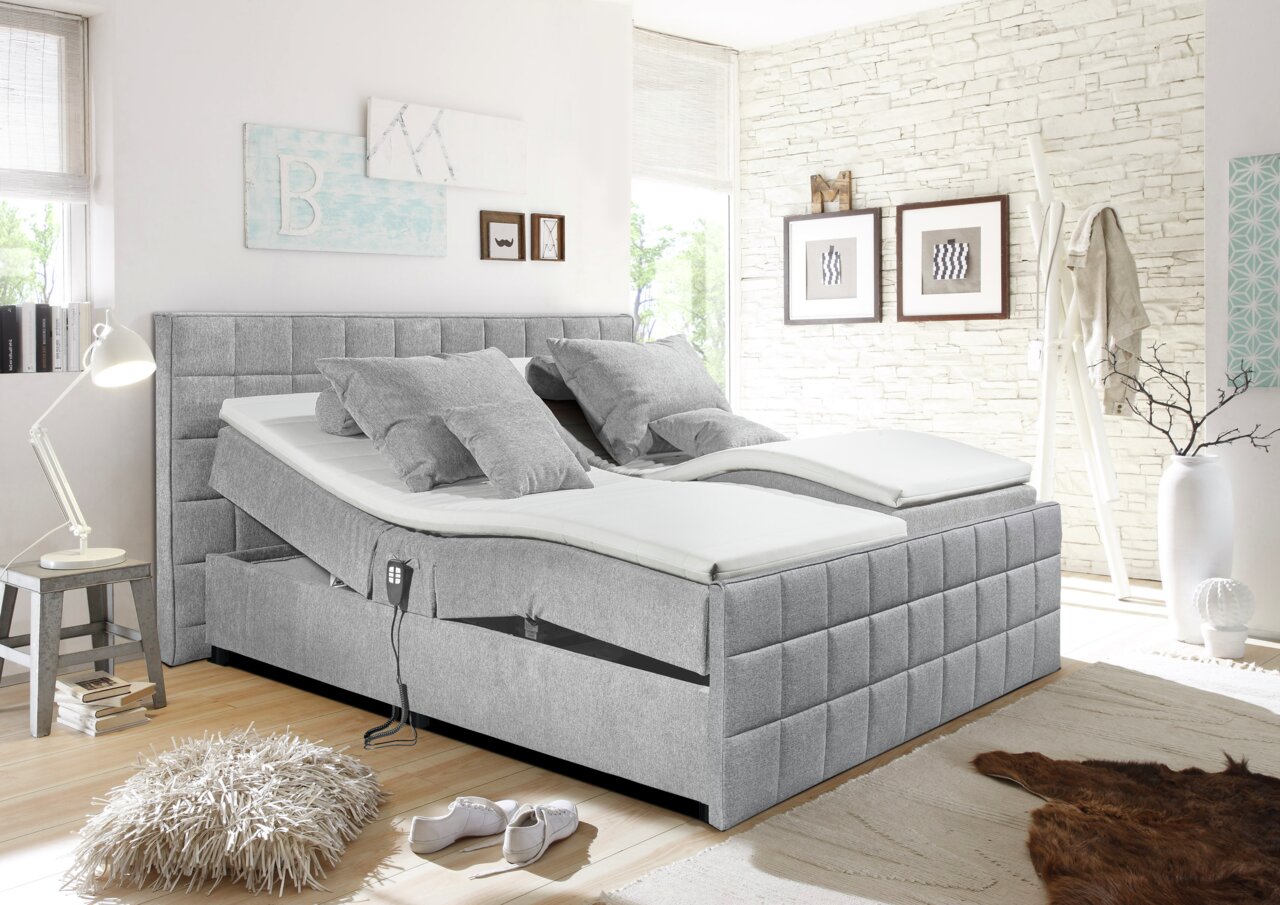 Graues Polsterbett mit verstellbaren Matratzen, seitliche Perspektive, in modernem Schlafzimmer mit heller Dekoration.