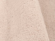 Nahaufnahme eines weichen, cremefarbenen Teppichs mit flauschiger Textur, perspektivisch von der Seite aufgenommen.