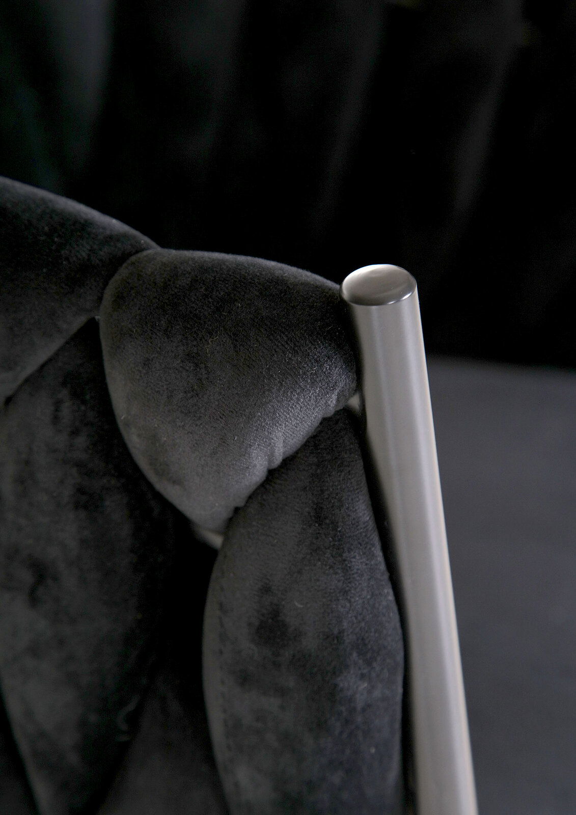 Nahaufnahme eines Sessels mit schwarzem, gepolstertem Stoff und einem silbernen Metallrahmen.