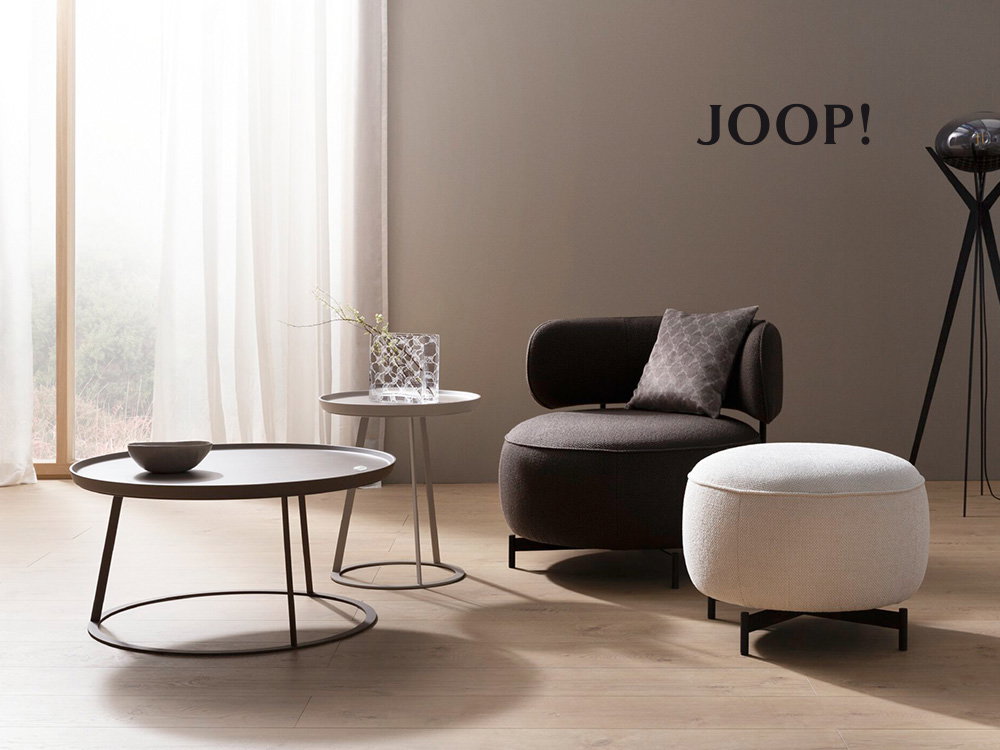 Elegantes JOOP! Interieur mit modernem Sessel, Hocker und stilvollen Beistelltischen in sanften Farbtönen.