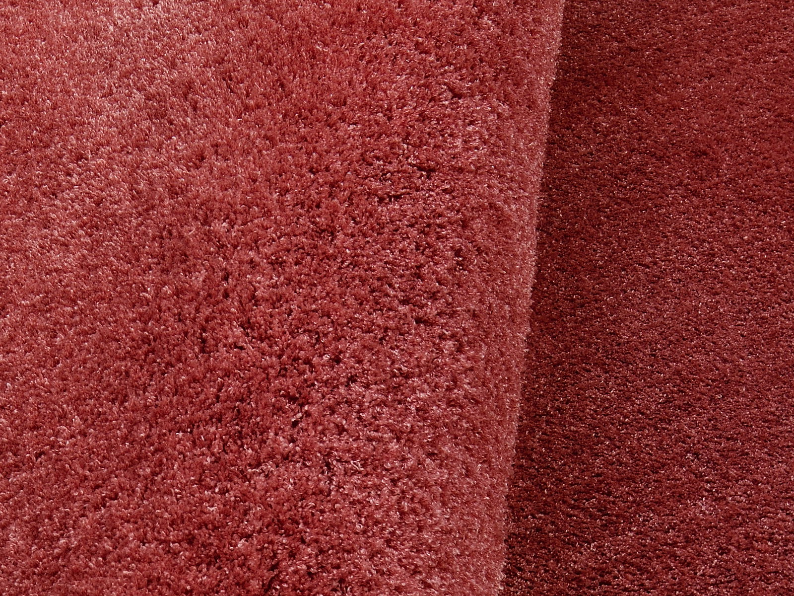Nahaufnahme eines runden, weichen, roten Teppichs mit flauschiger Textur, perspektivisch von oben fotografiert.