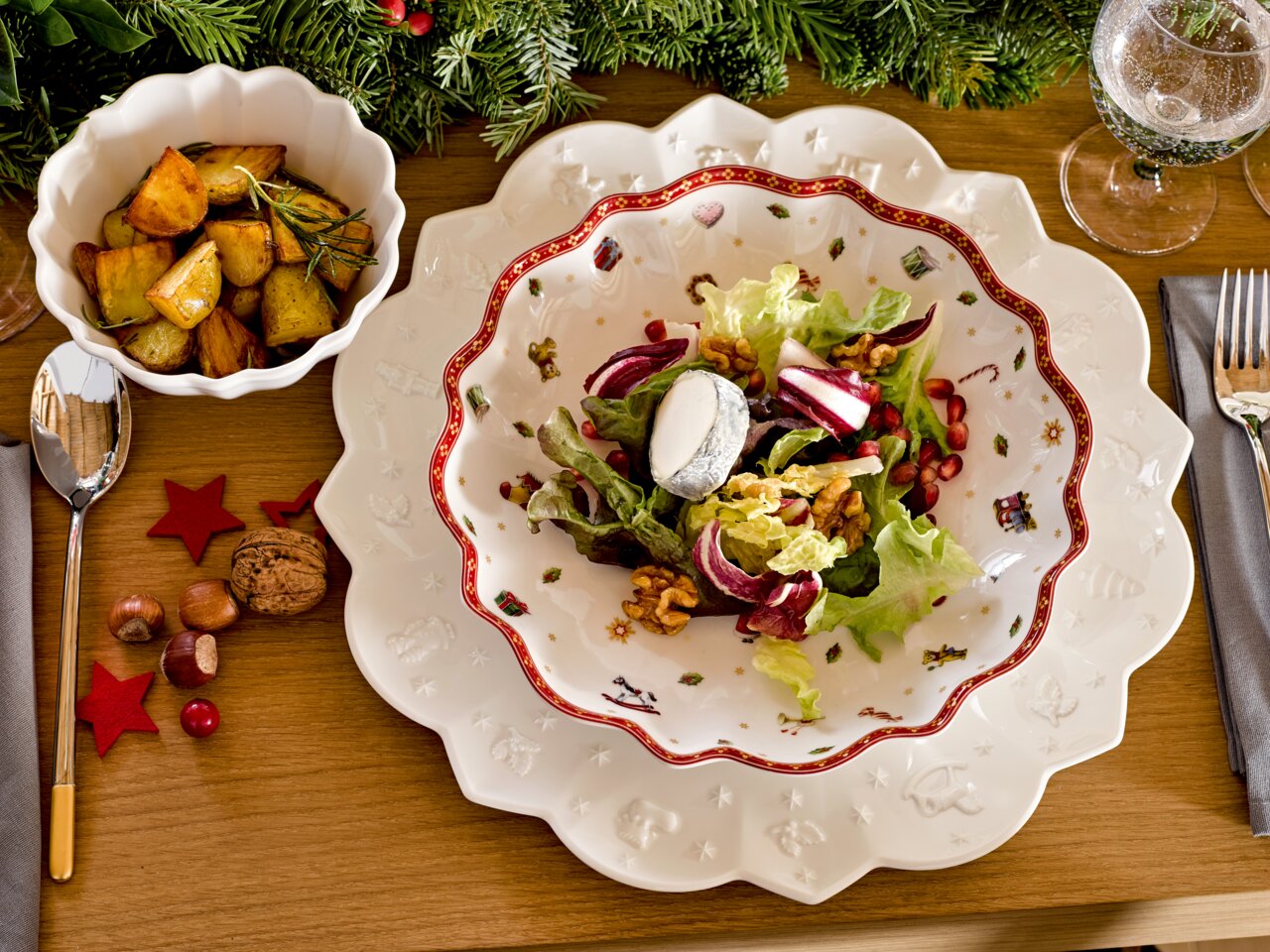 Villeroy & Boch Schale TOY'S DELIGHT Vogelperspektive auf einen festlich gedeckten Tisch mit einer kleinen Schale, gefüllt mit gerösteten Kartoffeln, und einem großen Teller mit Salat, dekoriert mit weihnachtlichen Motiven.