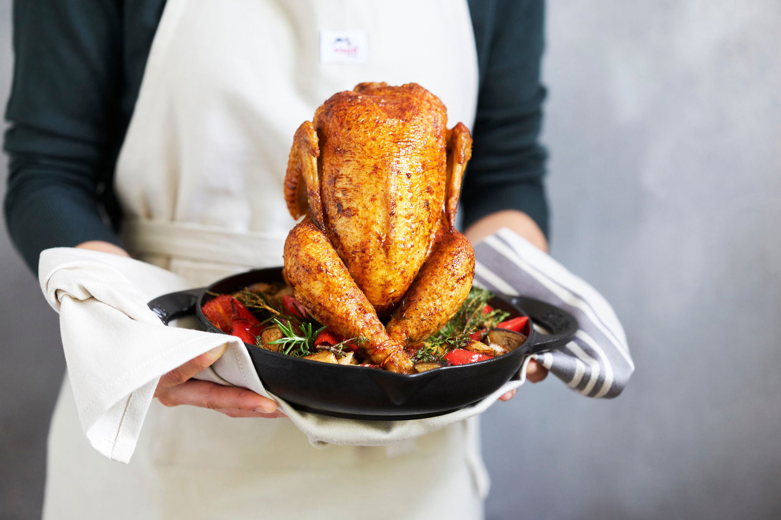 Person hält einen STAUB Hähnchenbräter mit einem goldbraun gebratenen Hähnchen und Gemüse, seitliche Perspektive.