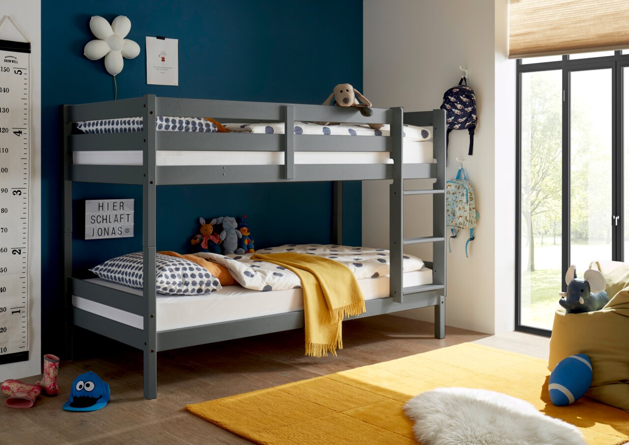 Graues Etagenbett in einem Kinderzimmer mit blauer Wand, dekoriert mit Kuscheltieren und bunten Kissen, seitliche Perspektive.