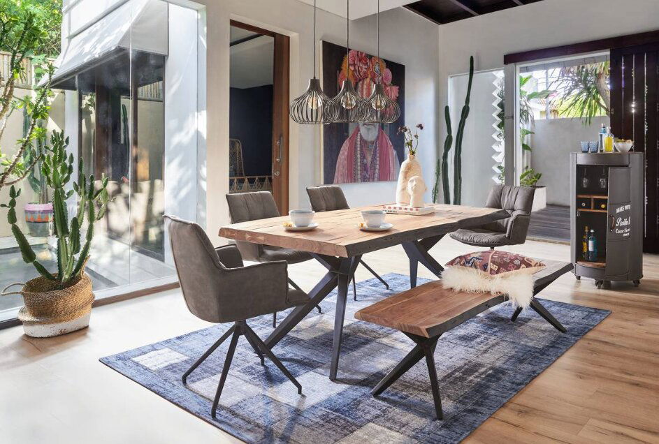 Esszimmer mit modernem Holztisch, umgeben von stilvollen Sesseln und einer Bank, aus der Perspektive des Raumes mit Blick auf große Fenster und Pflanzen.
