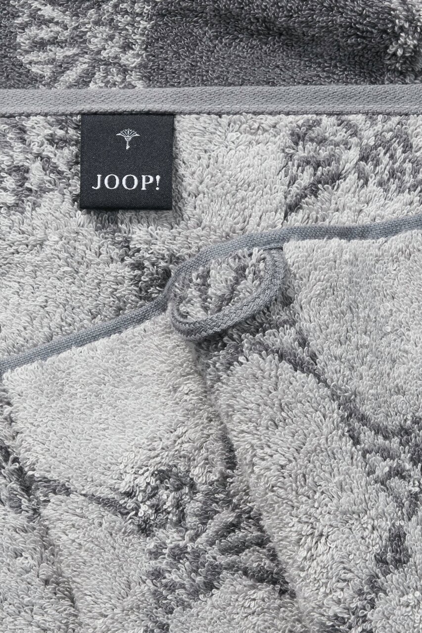 Close-up van een grijze saunadoek met bloemmotieven en een Joop-label.