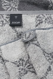 Close-up van een grijze saunadoek met bloemmotieven en een Joop-label.