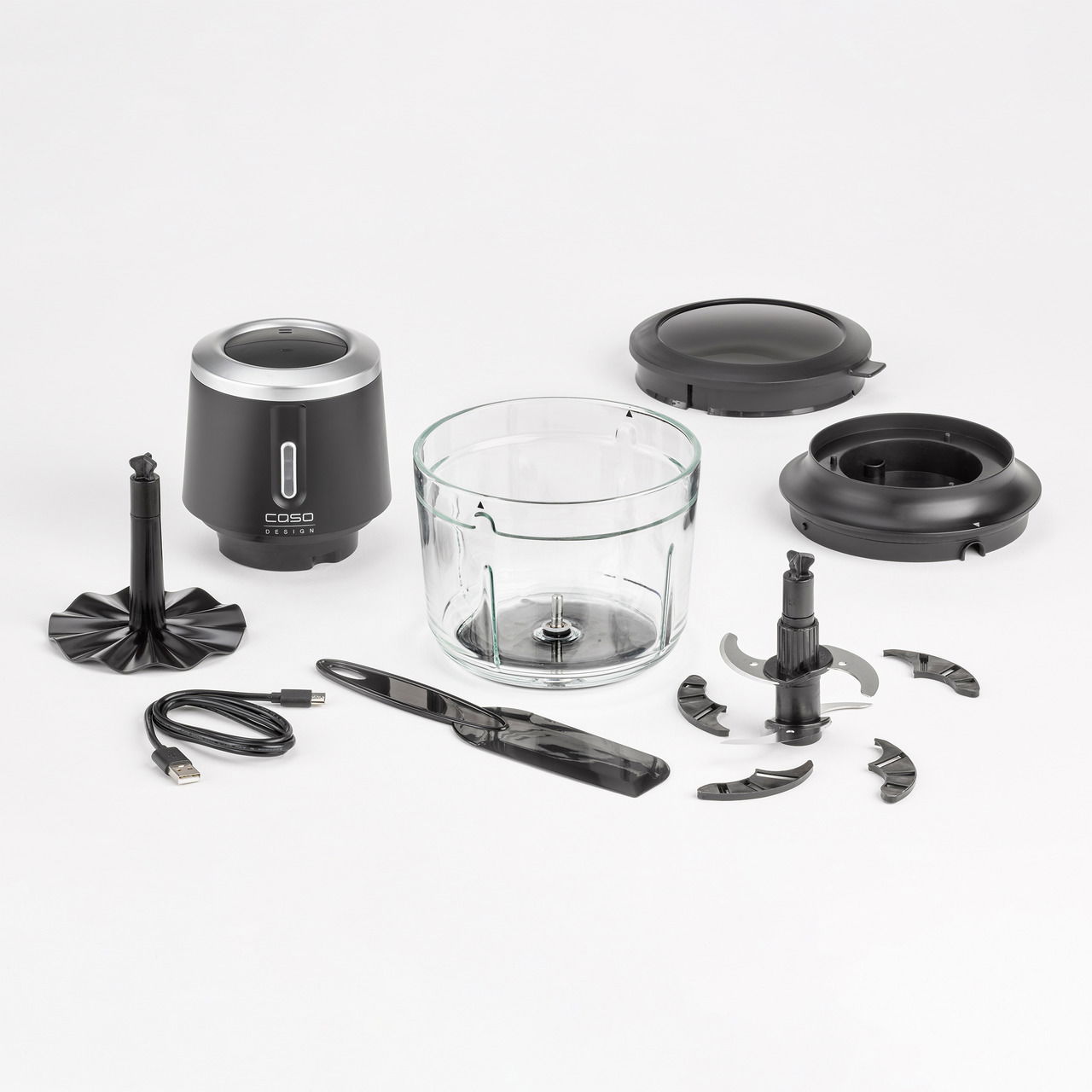 Akku-Multizerkleinerer mit Zubehör aus der Vogelperspektive, bestehend aus einem Glasbehälter, verschiedenen Klingenaufsätzen, einem schwarzen Motorblock und einem USB-Ladekabel.