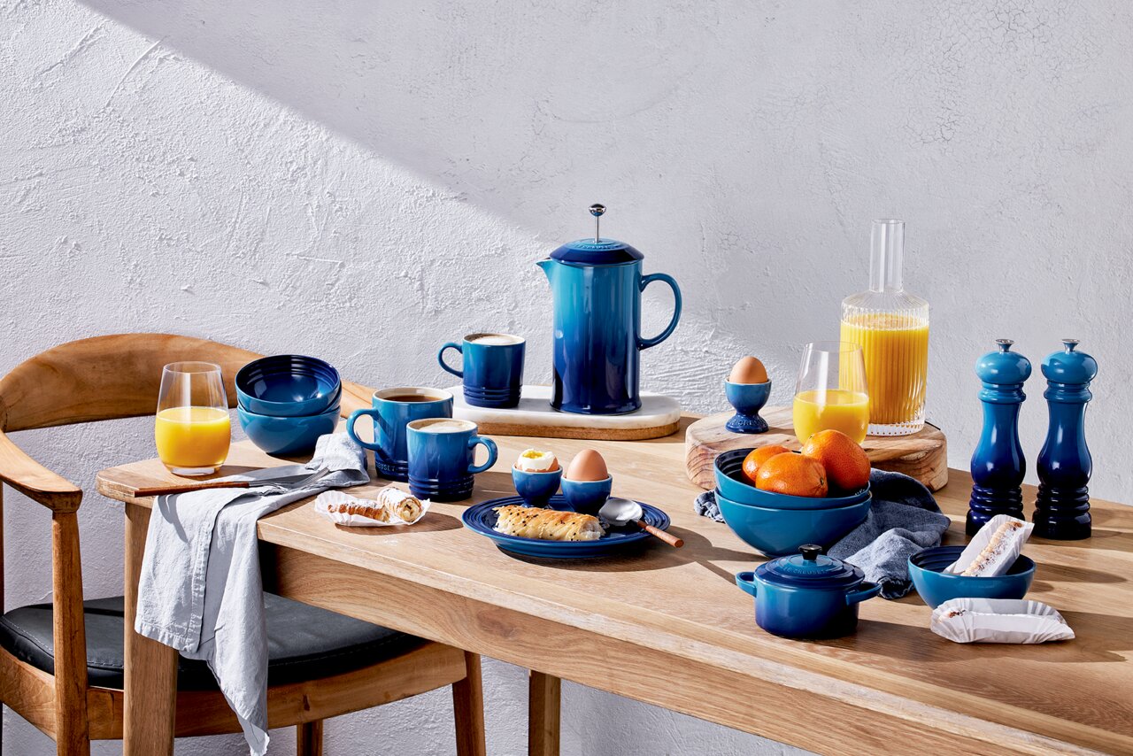 Frühstückstisch mit blauen Bechern und Geschirr in Azure-Farbe, von oben betrachtet.