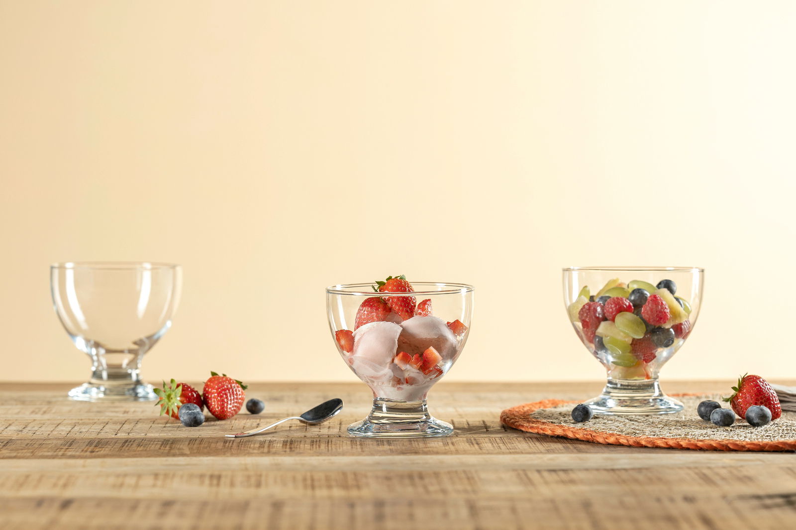 Leonardo Dessertschale JOE MONTANA Drei Dessertschalen aus Glas, gefüllt mit frischen Früchten und Eis, auf einem Holztisch. Perspektive von vorne.