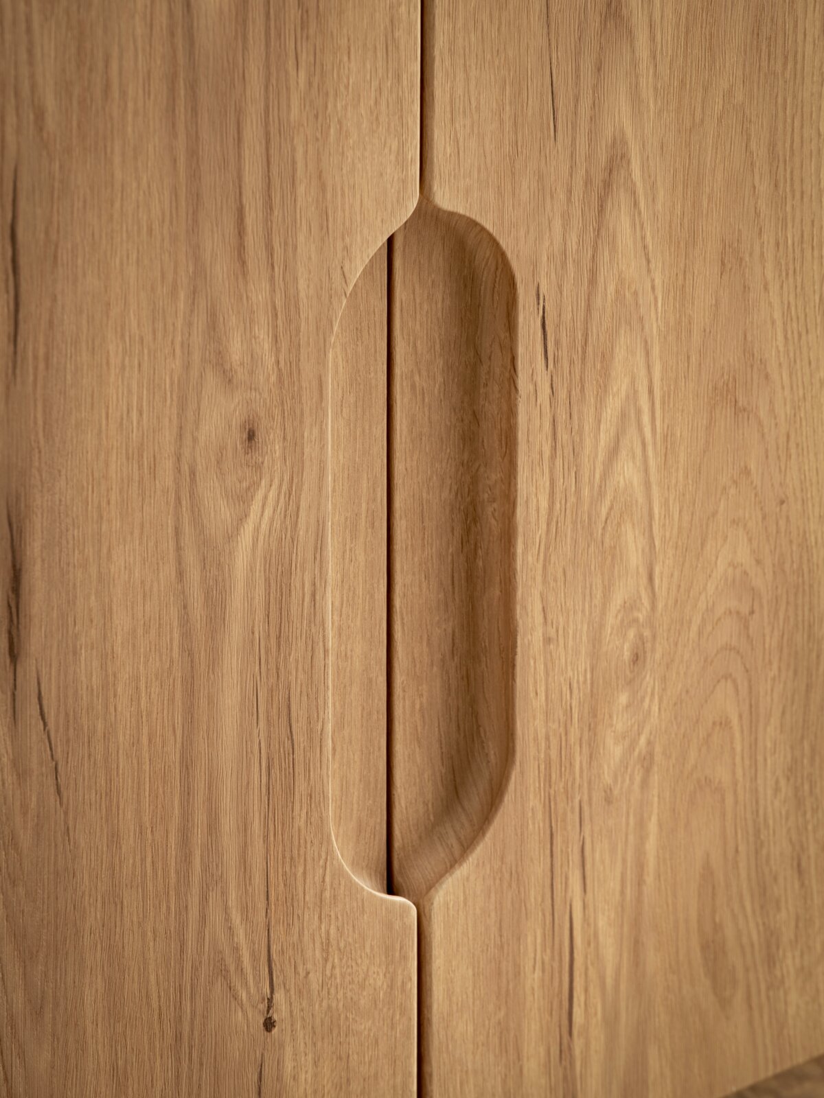 Nahaufnahme einer Holzschrankfront mit eingefrästem, vertikalem Griffdetail in der Mitte, Frontansicht