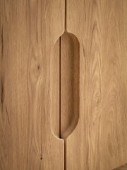 Nahaufnahme einer Holzschrankfront mit eingefrästem, vertikalem Griffdetail in der Mitte, Frontansicht