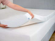 Nahaufnahme einer Person, die einen Tempur Topper Firm PRO PLUS SMARTCOOL auf eine Matratze legt, mit Fokus auf die Textur und das Design des Toppers.