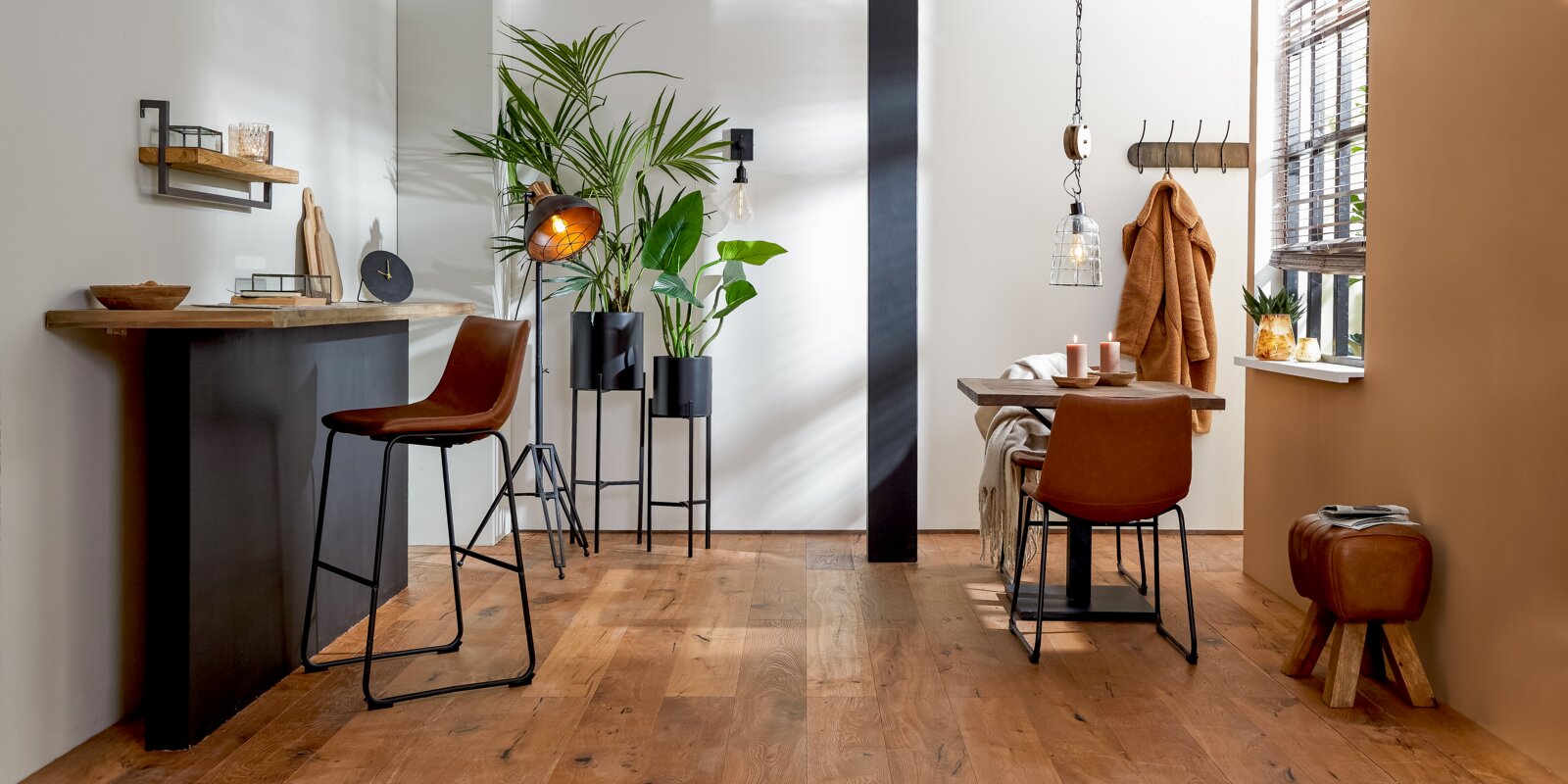 Moderne poef van bruin leer met houten poten, aan de zijkant geplaatst in een stijlvol ingerichte ruimte.