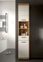 Hoher Badezimmer-Hochschrank in Eiche-Optik mit weißen Fronten, offenen Regalfächern und schwarzen Griffen, frontal aus leicht seitlicher Perspektive vor grauer Fliesenwand.