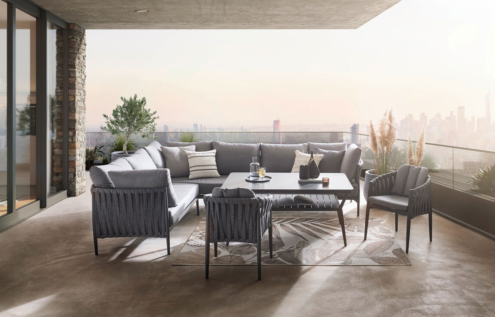 Moderner Gartentisch auf einer stilvollen Terrasse mit grauen Loungemöbeln und Blick auf die Skyline, seitliche Perspektive.