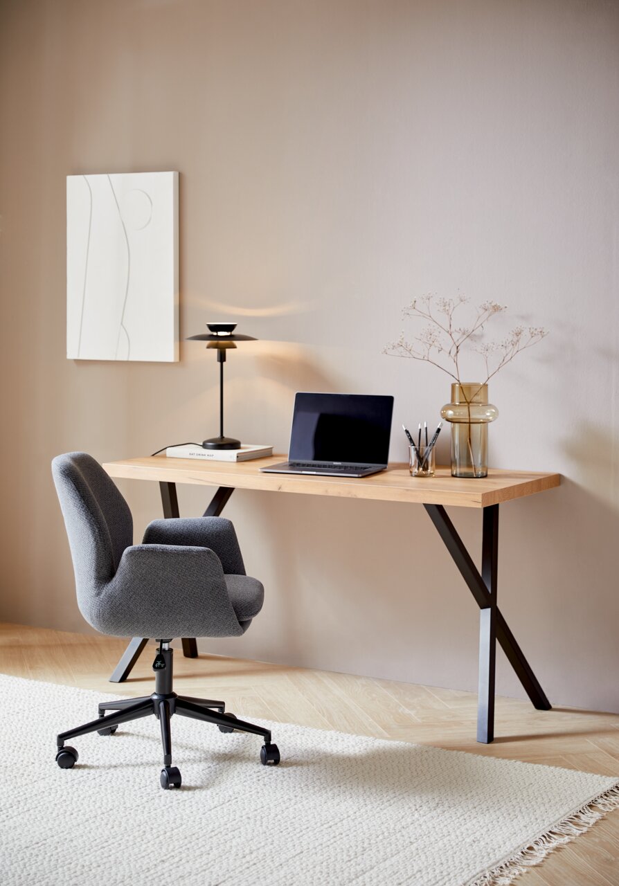 Moderner Schreibtisch mit Holzplatte und schwarzen Metallbeinen, darauf ein Laptop, eine Lampe und Dekorationen, seitliche Perspektive.
