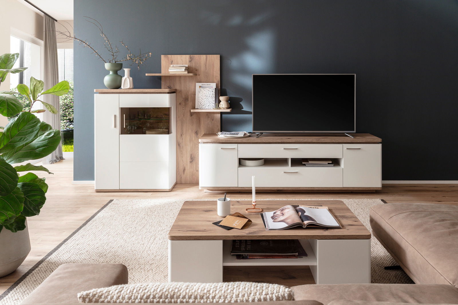 Moderne Wandkombination in einem stilvollen Wohnzimmer mit Holz- und Weißtönen, bestehend aus einem TV-Schrank, Regalen und einem Schrank, aus der Perspektive eines gemütlichen Wohnbereichs mit Sofa und Couchtisch.