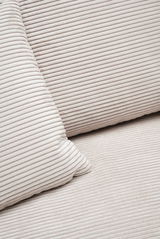 Nahaufnahme einer cremefarbenen, gerippten Stoffoberfläche mit Kissen, perspektivisch von oben betrachtet.