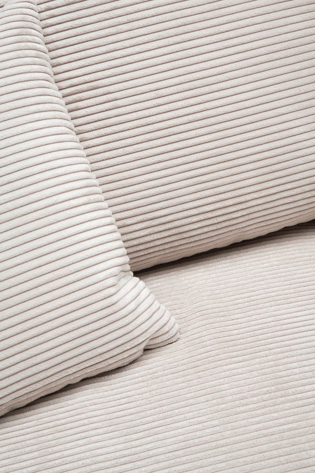 Nahaufnahme einer cremefarbenen, gerippten Stoffoberfläche mit Kissen, perspektivisch von oben betrachtet.