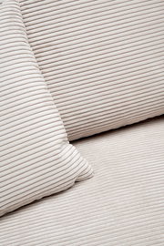 Nahaufnahme einer cremefarbenen, gerippten Stoffoberfläche mit Kissen, perspektivisch von oben betrachtet.