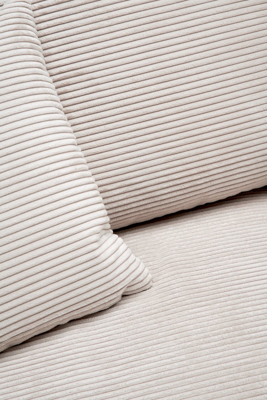 Nahaufnahme einer cremefarbenen, gerippten Stoffoberfläche mit Kissen, perspektivisch von oben betrachtet.