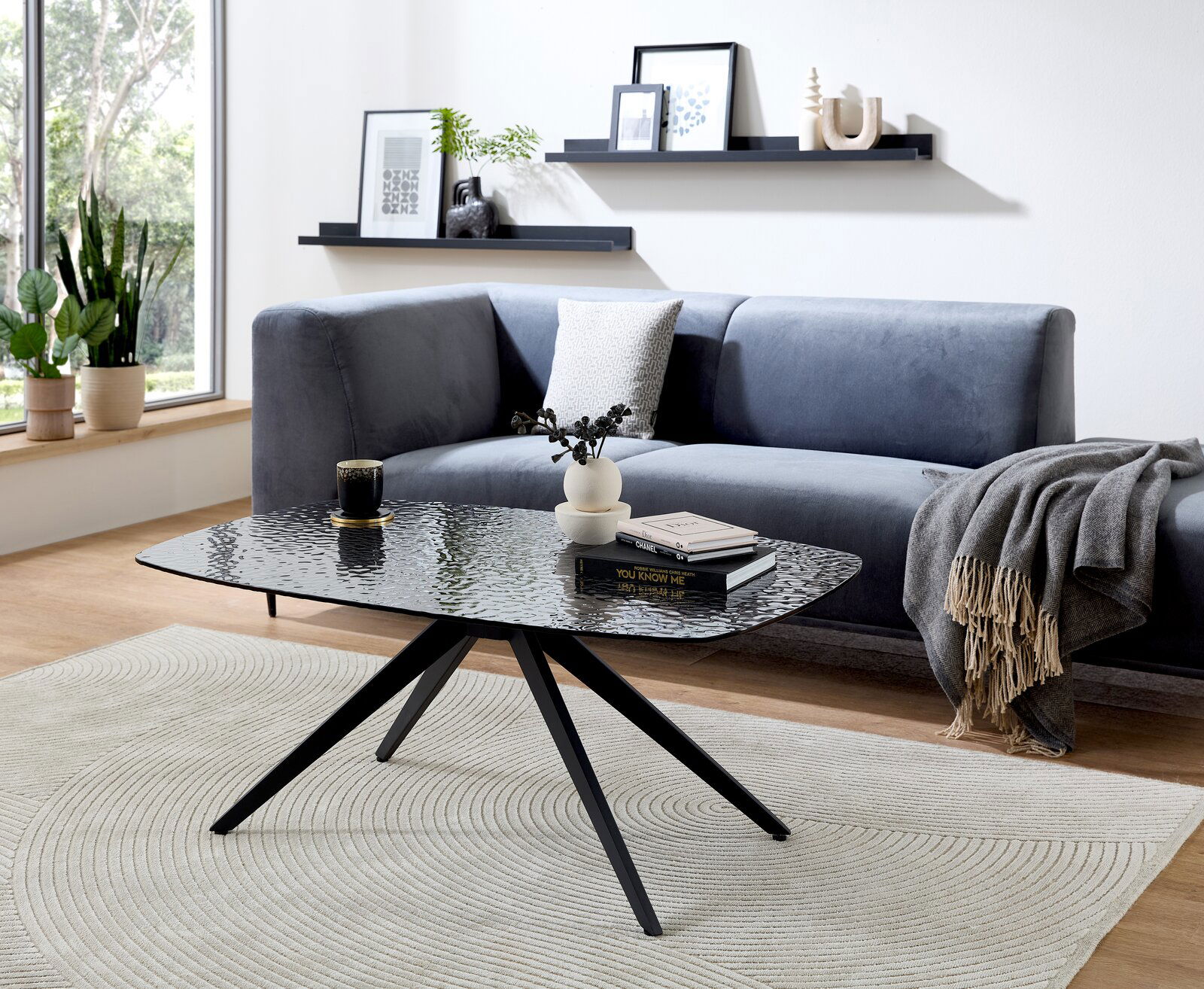 Z2 Couchtisch ELIAS Moderner Couchtisch mit schwarzer Glasplatte und Metallbeinen, im Wohnzimmer mit grauem Sofa und Dekorationen, seitliche Perspektive.