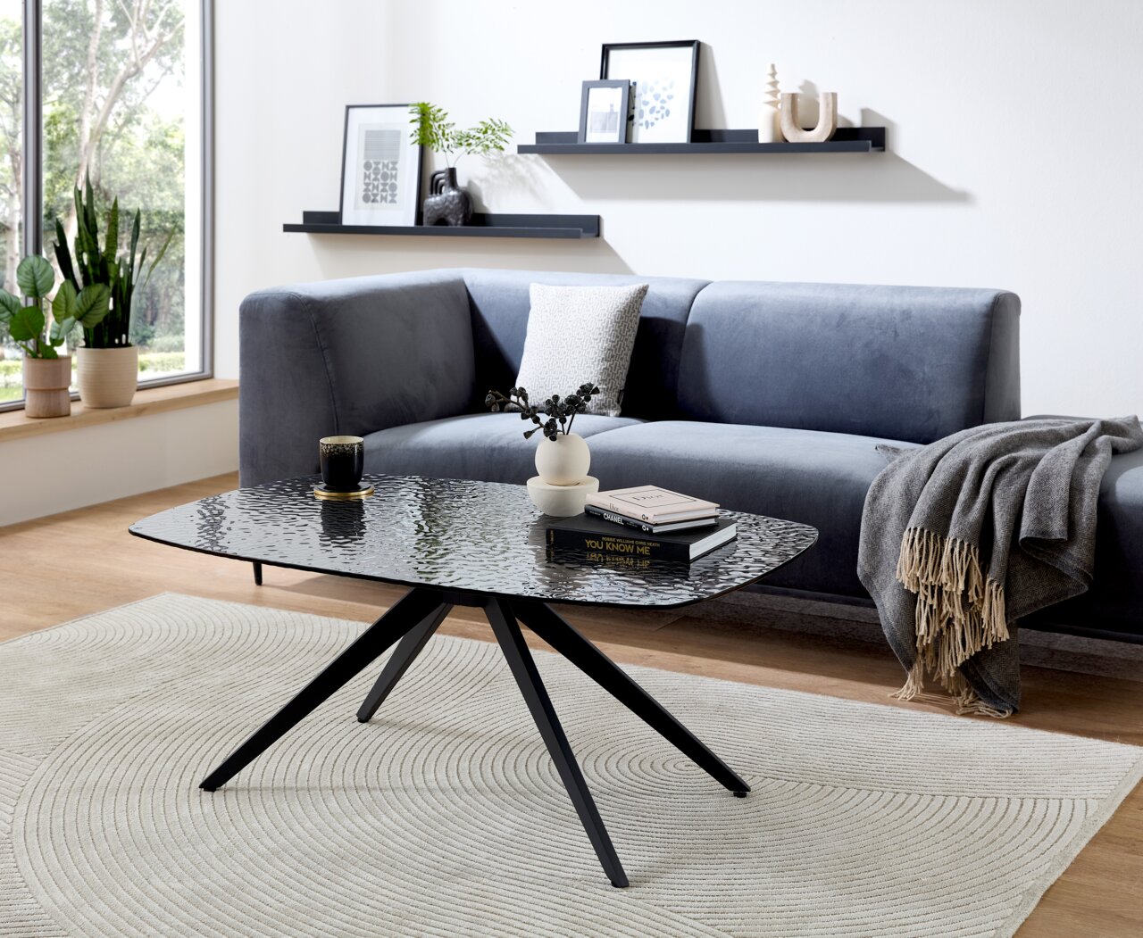 Moderner Couchtisch mit schwarzer Glasplatte und Metallbeinen, im Wohnzimmer mit grauem Sofa und Dekorationen, seitliche Perspektive.