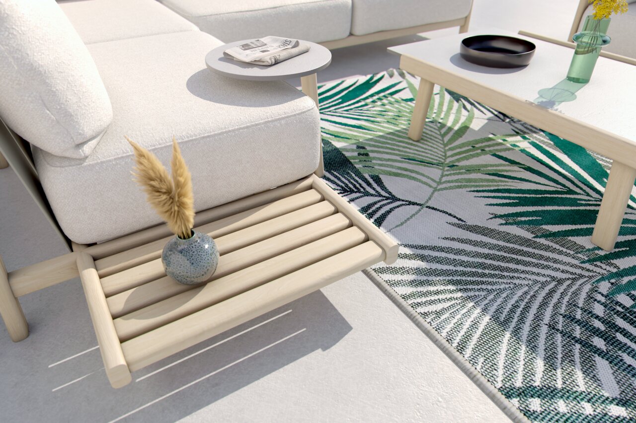 Loungeeckgarnitur mit hellem Holzgestell und weißen Polstern, seitliche Perspektive. Dekoriert mit einem kleinen Tisch, einer Vase und einem Teppich mit Blattmuster.