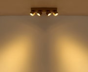 Deckenmontierte 4-flammige Spotleiste in mattem Gold mit warmweißem Lichtkegel an der Wand, Aufnahme aus leichter Untersicht (Blick nach oben)