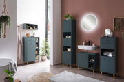 Modernes Badezimmer mit eleganten, dunkelblauen Regalen und Schränken, die auf Holzbeinen stehen. Die Perspektive zeigt eine stilvolle Anordnung der Möbel entlang einer Wand mit einem runden Spiegel und einem Waschbecken.
