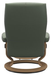 Achterkant van een groene fauteuil met houten frame en ronde voet.