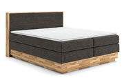 Boxspringbett mit grauem Stoffbezug und Holzrahmen, seitliche Perspektive