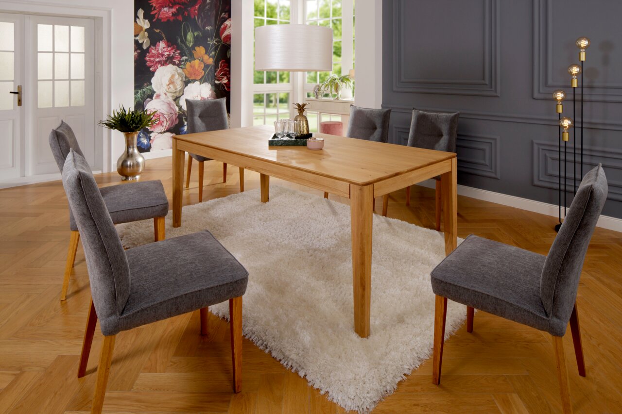 Moderner Esstisch aus Holz mit sechs grauen Stühlen in einem stilvoll eingerichteten Esszimmer, Perspektive von schräg vorne.