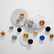 Verschiedene Deckelknäufe aus Edelstahl in verschiedenen Formen und Farben, von oben betrachtet, auf einer weißen Oberfläche arrangiert.