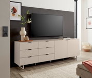 Modernes, hellbeiges TV-Lowboard mit Schubladen und Türen auf schlanken Metallfüßen, mit Fernseher und Deko im Wohnzimmer, frontale Perspektive.