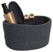 Dunkelgrauer Aufbewahrungskorb aus geflochtenem Material, gefüllt mit einer Sprühflasche, einer Haarbürste und zwei goldenen Haarklammern, seitliche Perspektive.