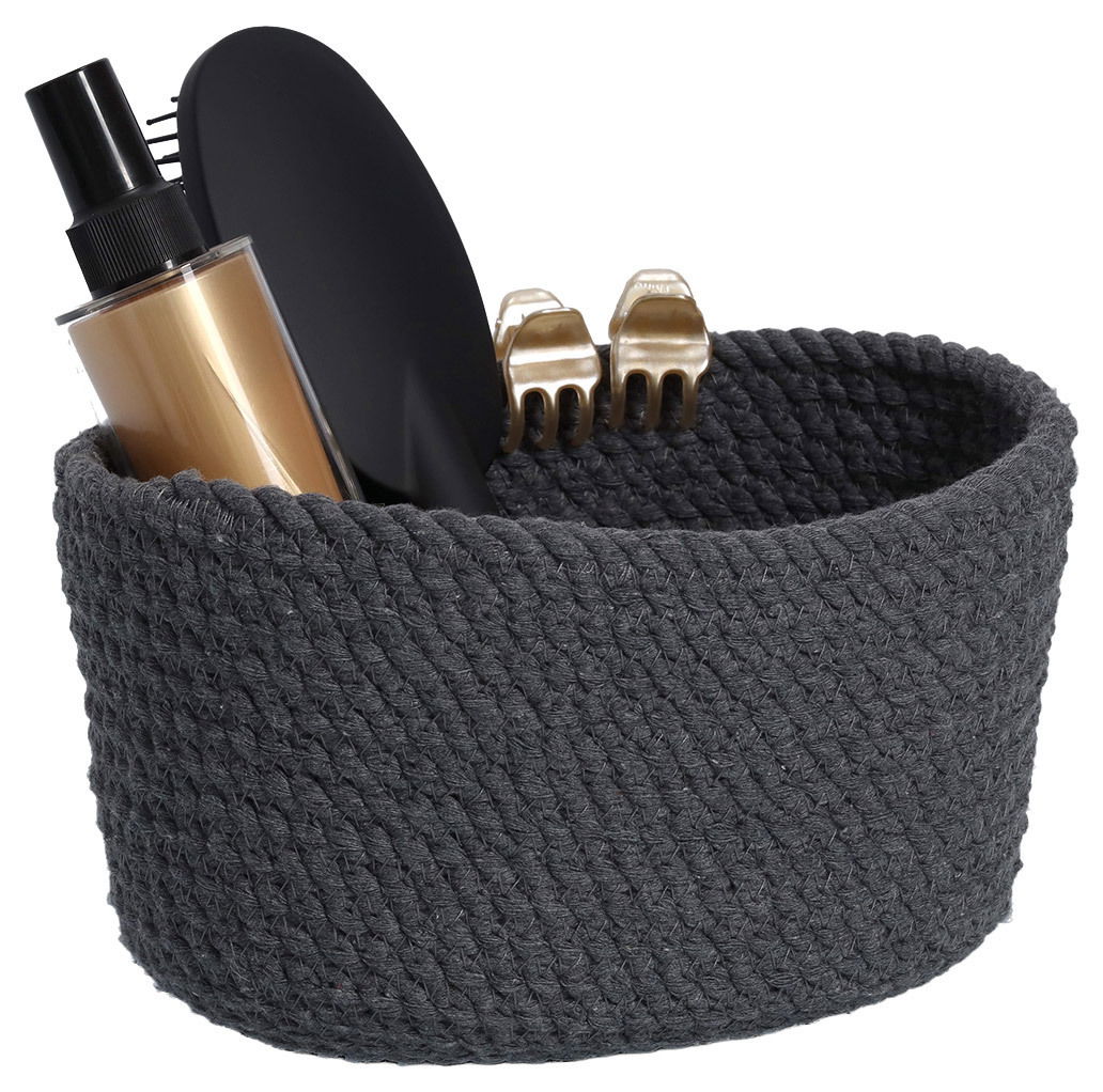 Dunkelgrauer Aufbewahrungskorb aus geflochtenem Material, gefüllt mit einer Sprühflasche, einer Haarbürste und zwei goldenen Haarklammern, seitliche Perspektive.