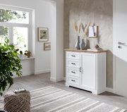 Weiße Kommode mit Holzplatte und vier Schubladen, seitliche Perspektive, dekoriert mit Vasen und Büchern, in einem hellen Raum mit Pflanzen und Wandkunst.