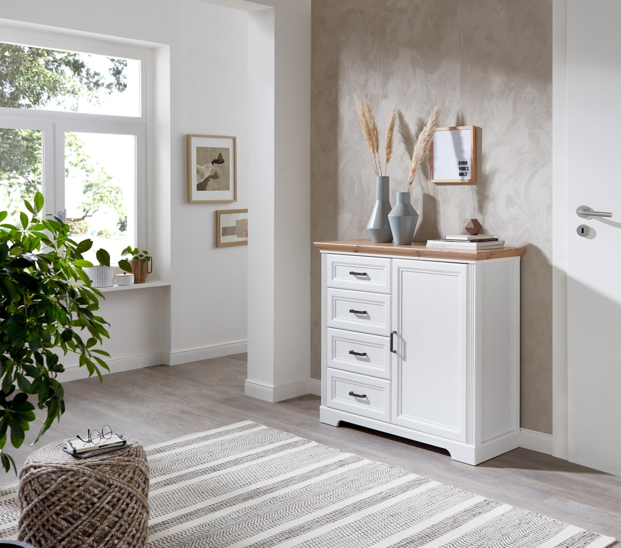 Landscape Kommode JUDITH Weiße Kommode mit Holzplatte und vier Schubladen, seitliche Perspektive, dekoriert mit Vasen und Büchern, in einem hellen Raum mit Pflanzen und Wandkunst.